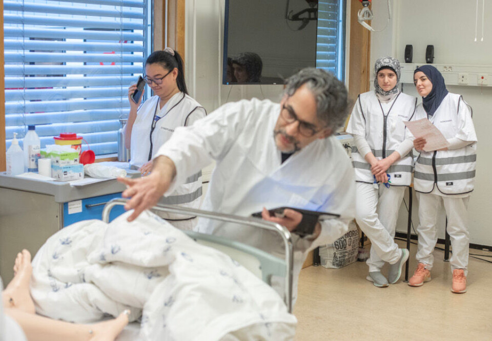 Gjennom mye av øvelsen holder bioingeniørstudentene Makka Imaeve (til venstre) og Shaymaa Fayad seg i bakgrunnen, akkurat slik de ville gjort i en reell akuttsituasjon. Fra sin post får de rikelig med tid til å observere hva de andre yrkesgruppene gjør, og hvordan de jobber. I telefonen videreformidler sykepleierstudent Hedda Enger beskjeder fra lege og instruktør David Jahanlu. Foto: Fredrik Naumann