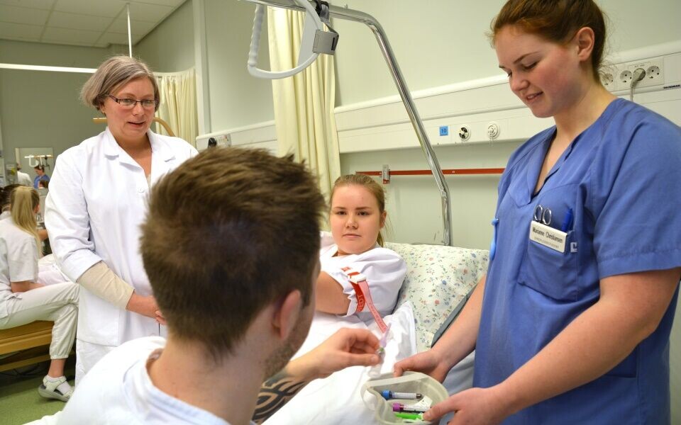 Laboratoriekonsulent Randi Rekkebo følger med på «elevene» sine – sykepleierstudentene Maren Dalen (i senga), Kjetil Kvaal og Marianne Christiansen. (Foto: Bjørnar Leknes, Nord universitet)