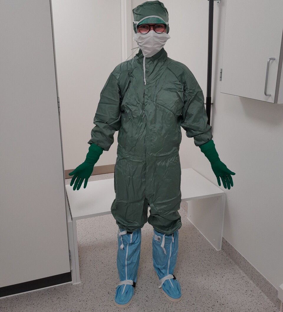 Billede 4: Arbejdsuniformen i renrum er noget mere omstændig end en standard hospitalskittel. På billedet ses den grønne renrumsdragt, de blå renrumsstøvler, maske, handsker og hårnet. Dette er dog kun toppen af isbjerget. Under er et sæt langærmet renrumsundertøj, et ekstra sæt handsker og to par sokker. Det tager omkring 15 min at blive fuldt omklædt og kræver både præcision og balance. Påkledning til renrom