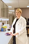 En kvinne i hvit labfrakk står ved en laboratoriebenk med en liten eske og annet utstyr i bakgrunnen.
