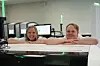 To personer står med albuene på en stor laboratoriemaskin i et rom med dataskjermer og utstyr.