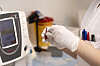 En person med hansker holder en liten prøve ved en analysemaskin på et laboratorium.