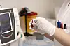 En person med hansker holder en liten prøve ved en analysemaskin på et laboratorium.