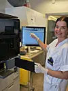 Laborant i hvit drakt peker på skjermen til en analysemaskin i et laboratorium.