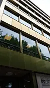 Skrått sett glass- og metallfasade på en moderne bygning med refleksjoner av trær og himmel.