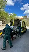 To personer i grønne vernedrakter laster en båre inn i en gul ambulanse ved veien.