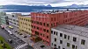 Fargerike sykehusbygg langs en gate ved sjøen, med biler og fjell i bakgrunnen.