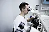 Person i hvit frakk ser gjennom et mikroskop i et laboratorium.