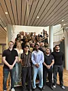Stor gruppe mennesker står samlet på en trapp i et lyst atrium med moderne arkitektur.
