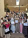 Stor gruppe mennesker poserer i en trappeoppgang med blomster og diplomer.