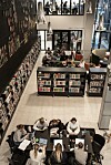 Studenter arbeider ved bord i et lyst bibliotek med bokhyller, store vinduer og høye lamper.