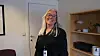 Smilende kvinne med briller står i et lyst kontormiljø med hyller i bakgrunnen.