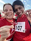 To smilende løpere i røde trøyer poserer med startnummer 107 og en medalje.