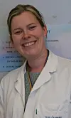 Smilende helsearbeider i hvit frakk foran en norsk informasjonsplakat.