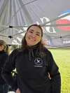 Smilende kvinne i mørk genser står under et telt på en gresslette.