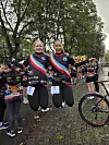 To smilende deltakere i fargerike drakter står ved målområdet med andre deltakere rundt seg.