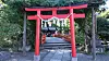 Rød torii-port foran en japansk helligdom, omgitt av trær og steinlagt gangvei.