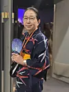 Kvinne i mørk tradisjonell drakt med vifte står i en inngang. Yukata