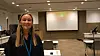 Smilende kvinne i en konferansesal med projektorlerret og møtebord.
