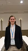 Person med mørk blazer og navneskilt står i et lyst møterom.