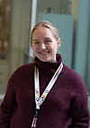 Smilende kvinne i mørkerød genser med adgangskort-bånd rundt halsen.